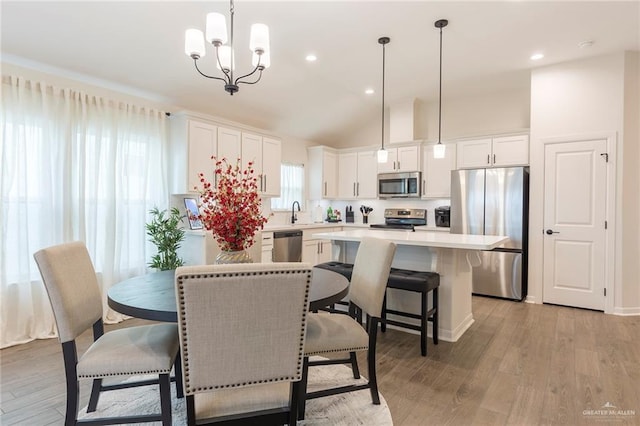 dining area featuring an inviting chandelier, sink, light hardwood / wood-style flooring, and vaulted ceiling