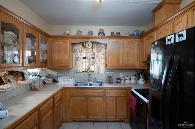 kitchen featuring extractor fan, sink, black appliances, light tile patterned floors, and tile countertops