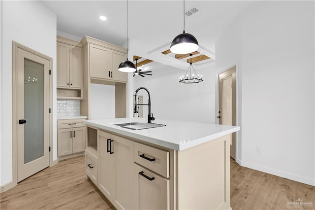 kitchen with sink, hanging light fixtures, cream cabinetry, a kitchen island with sink, and light wood-type flooring