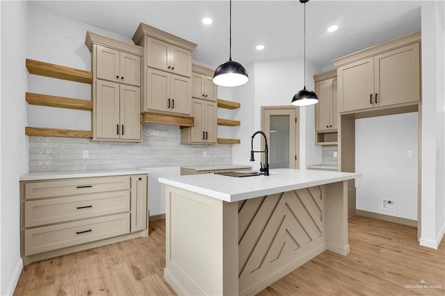 kitchen with decorative backsplash, pendant lighting, light hardwood / wood-style flooring, and an island with sink