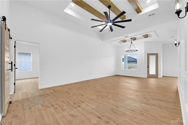 unfurnished living room with beam ceiling, a barn door, light hardwood / wood-style floors, and ceiling fan with notable chandelier