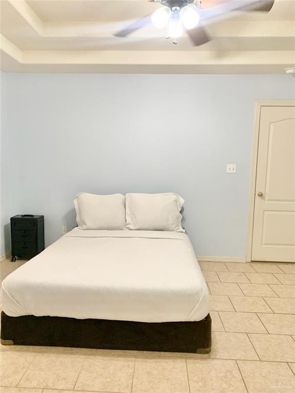 bedroom with a raised ceiling, light tile patterned floors, and ceiling fan