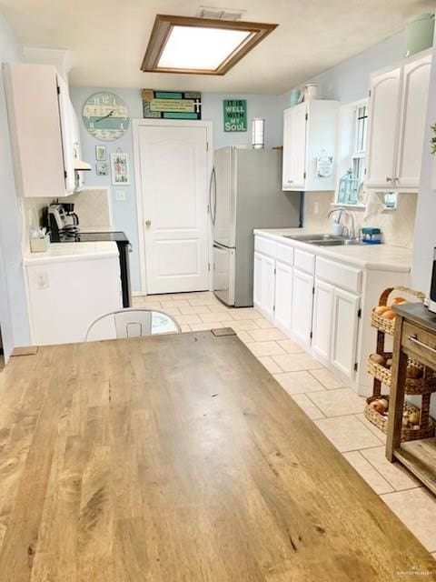 kitchen featuring sink, stainless steel refrigerator, white cabinets, decorative backsplash, and exhaust hood