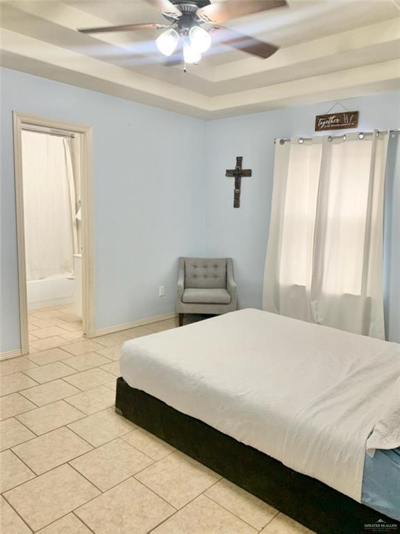 tiled bedroom featuring ceiling fan, ensuite bathroom, and a raised ceiling