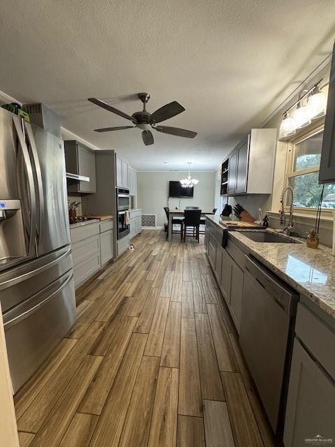 kitchen with light stone countertops, sink, stainless steel appliances, wood-type flooring, and ceiling fan with notable chandelier