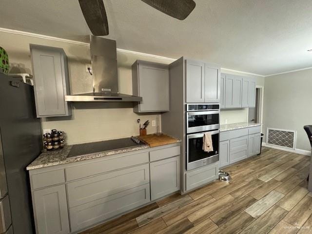 kitchen with light hardwood / wood-style floors, stainless steel appliances, ceiling fan, wall chimney range hood, and gray cabinets