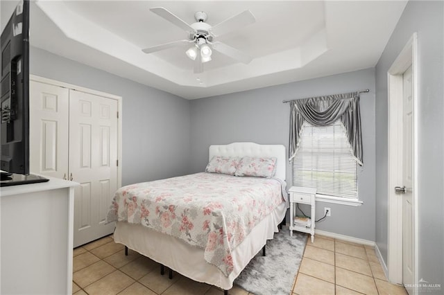 bedroom featuring a raised ceiling, light tile patterned floors, a closet, baseboards, and ceiling fan