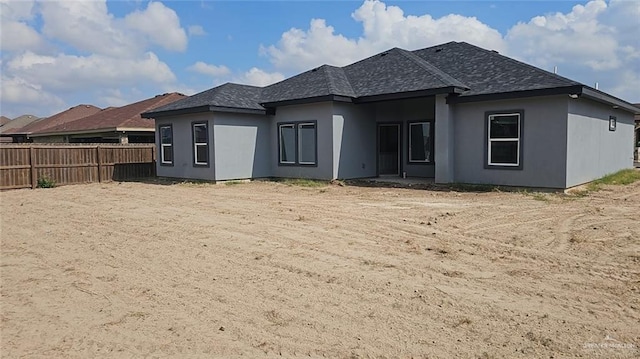 rear view of property featuring roof with shingles, fence, and stucco siding