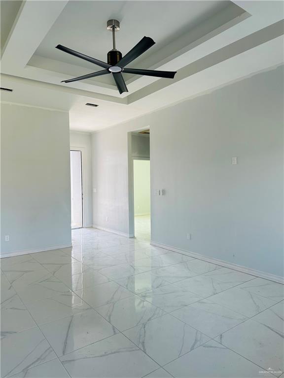 empty room featuring a tray ceiling, marble finish floor, and baseboards