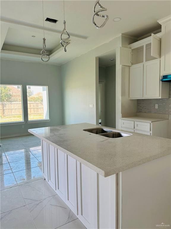 kitchen with a kitchen island with sink, a raised ceiling, decorative light fixtures, and white cabinetry