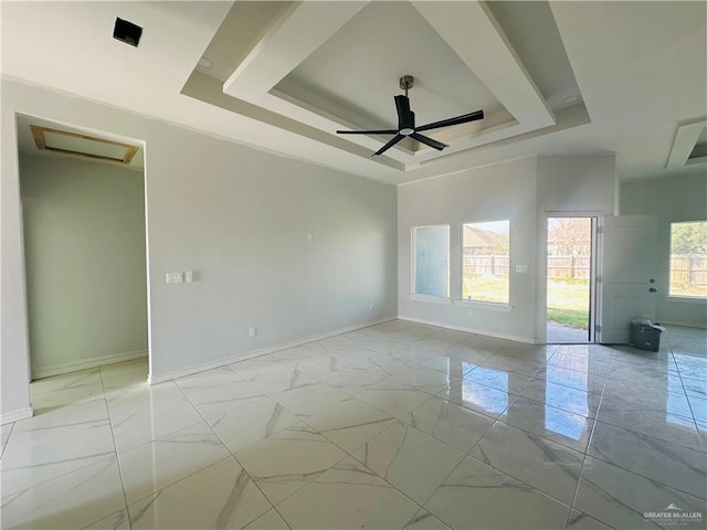 empty room featuring marble finish floor, a raised ceiling, attic access, and baseboards