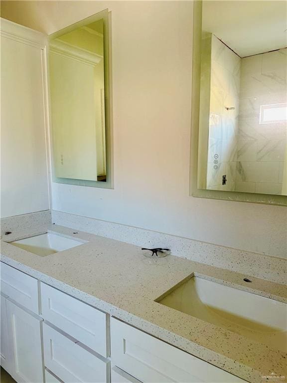 bathroom featuring double vanity, a tile shower, and a sink