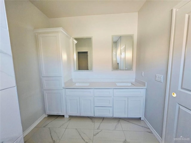 full bath with double vanity, marble finish floor, baseboards, and a sink