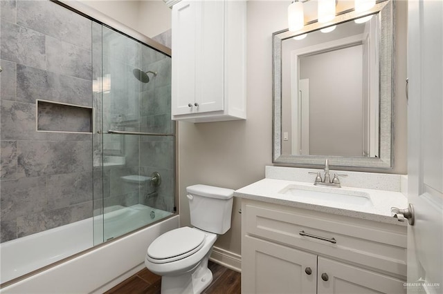 full bath featuring bath / shower combo with glass door, wood finished floors, vanity, and toilet