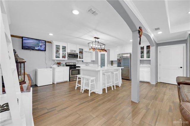 kitchen featuring a breakfast bar, hanging light fixtures, light hardwood / wood-style flooring, white cabinetry, and stainless steel appliances