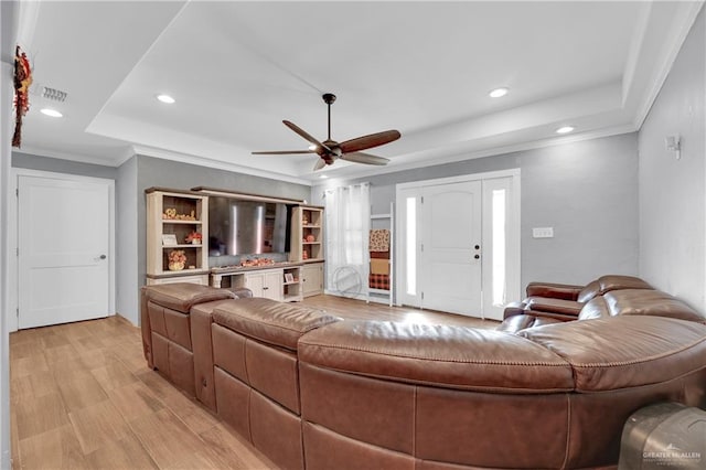 living room featuring ceiling fan, ornamental molding, a tray ceiling, and light hardwood / wood-style flooring