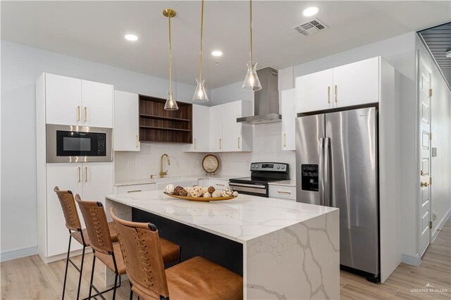 109 E Parade Dr Unit G, South Padre Island, TX 78597 - kitchen featuring a center island, stainless steel appliances, wall chimney range hood, pendant lighting, and light wood-type flooring
