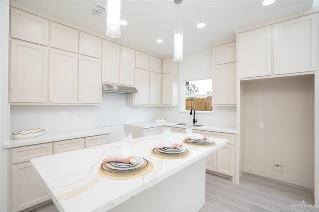 kitchen featuring sink, a center island, pendant lighting, light stone countertops, and white cabinets