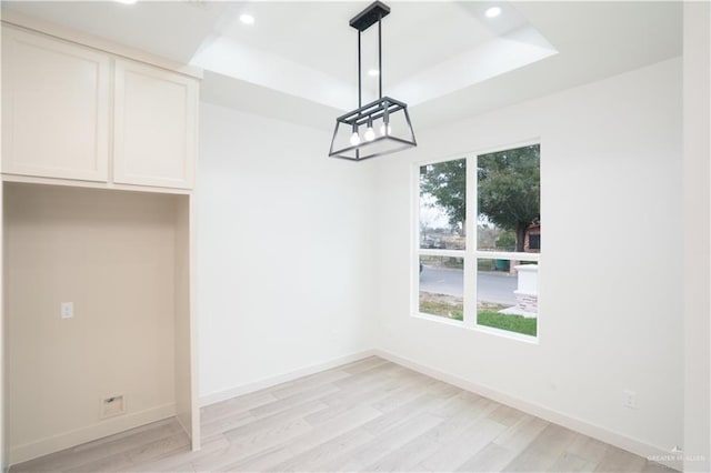 unfurnished dining area with a raised ceiling and light hardwood / wood-style floors