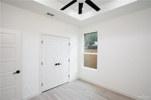 unfurnished bedroom featuring a closet, light hardwood / wood-style flooring, a raised ceiling, and ceiling fan