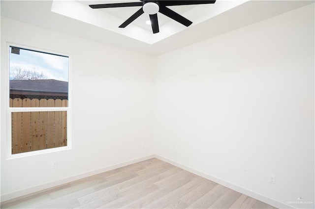 spare room with a tray ceiling, light hardwood / wood-style flooring, and ceiling fan