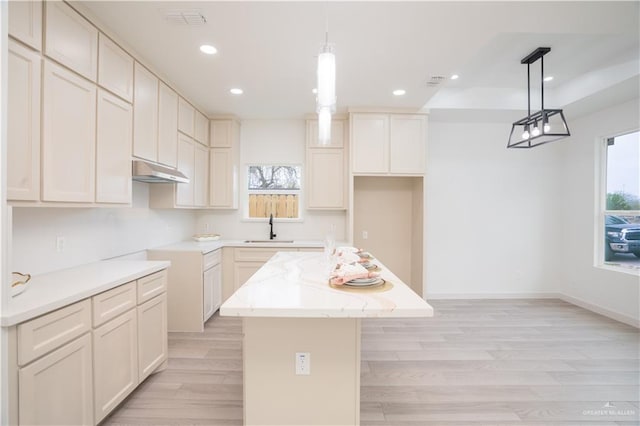 kitchen featuring sink, a kitchen island, pendant lighting, light stone countertops, and light hardwood / wood-style floors