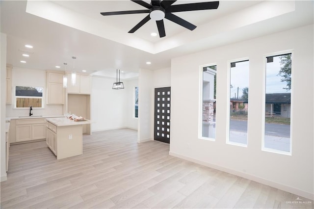 kitchen with sink, hanging light fixtures, a center island, a tray ceiling, and light wood-type flooring