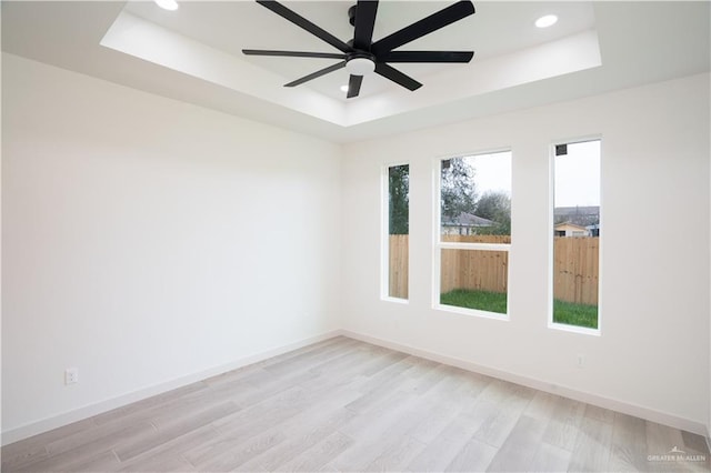 empty room featuring a tray ceiling, ceiling fan, and light wood-type flooring