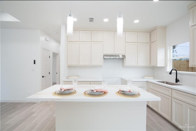 kitchen with hanging light fixtures, a kitchen island, sink, and white cabinets