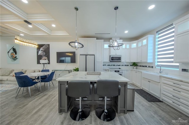 kitchen with coffered ceiling, a kitchen island, light wood-style flooring, stainless steel appliances, and white cabinetry