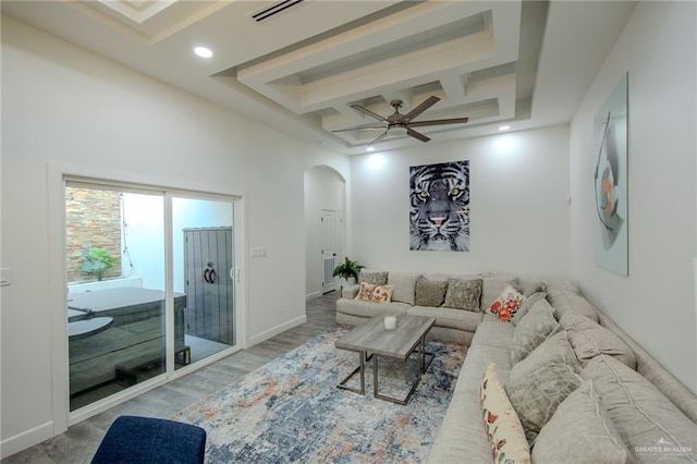 living area featuring visible vents, coffered ceiling, wood finished floors, arched walkways, and baseboards