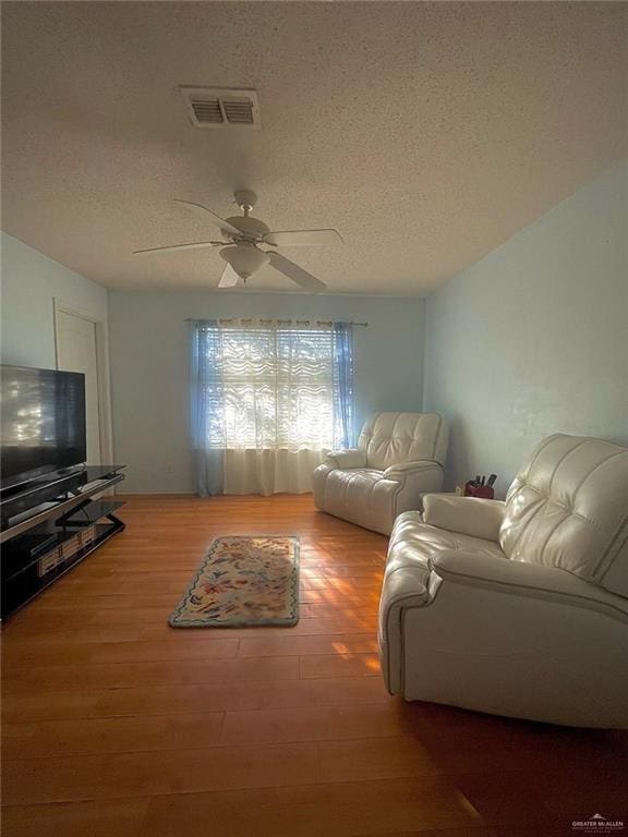 living room featuring ceiling fan, wood finished floors, a textured ceiling, and visible vents