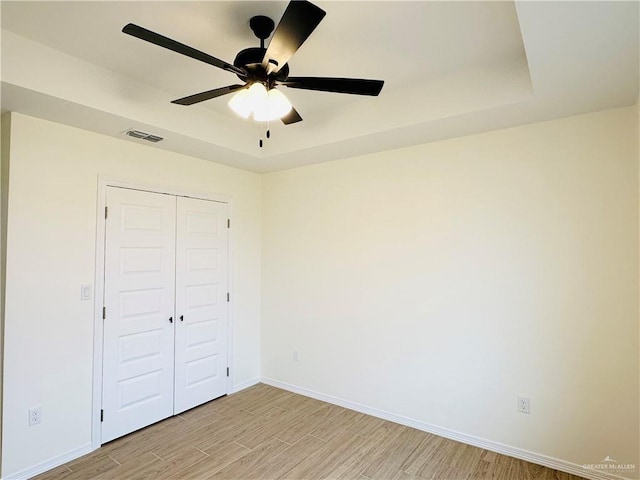 unfurnished bedroom featuring ceiling fan, a tray ceiling, and a closet