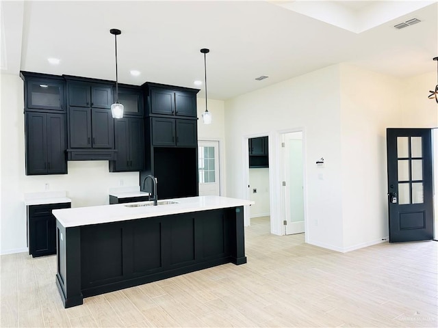 kitchen with hanging light fixtures, sink, a center island with sink, and light wood-type flooring