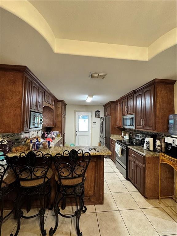 704 S 17th St, Hidalgo, TX 78557 - kitchen with appliances with stainless steel finishes, decorative backsplash, light tile patterned floors, a peninsula, and a tray ceiling
