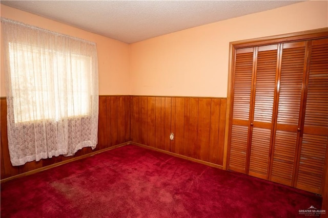 unfurnished bedroom with a textured ceiling, carpet floors, a closet, and wooden walls