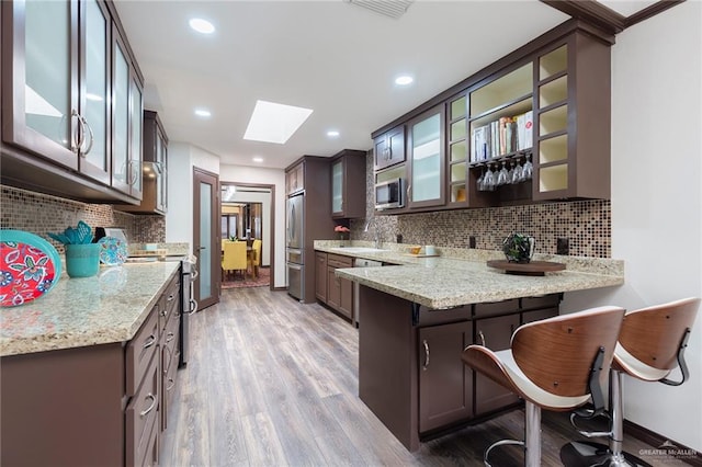 kitchen with light wood-type flooring, kitchen peninsula, stainless steel appliances, and a skylight