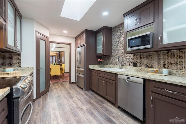 kitchen featuring sink, a skylight, light hardwood / wood-style flooring, light stone counters, and stainless steel appliances