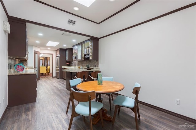 dining space featuring dark hardwood / wood-style floors, ornamental molding, and a skylight