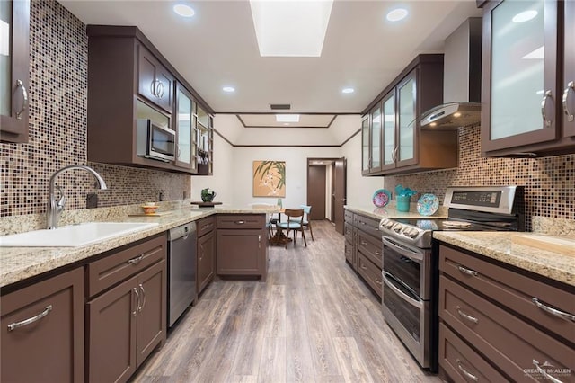 kitchen featuring light stone countertops, wall chimney exhaust hood, stainless steel appliances, sink, and hardwood / wood-style flooring