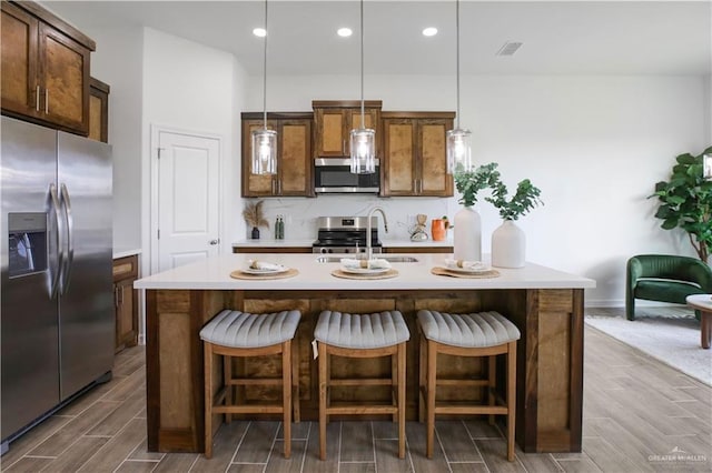 kitchen featuring a center island with sink, stainless steel appliances, decorative light fixtures, sink, and a kitchen bar