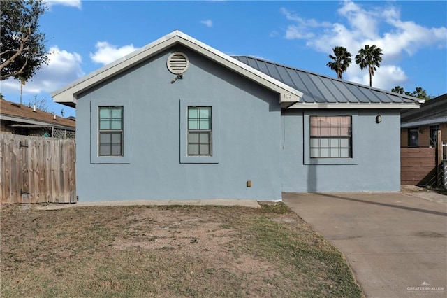 view of side of property featuring fence, metal roof, and stucco siding