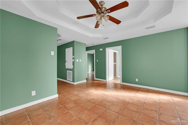 spare room with a raised ceiling, visible vents, a ceiling fan, light tile patterned flooring, and baseboards