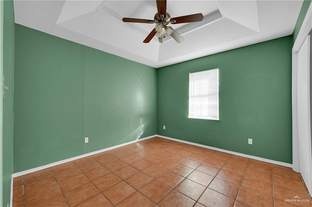 unfurnished room featuring a tray ceiling, tile patterned flooring, ceiling fan, and baseboards