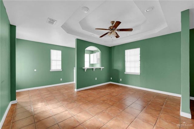 tiled empty room with a raised ceiling, plenty of natural light, and baseboards