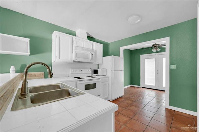 kitchen with white appliances, baseboards, white cabinets, tile countertops, and a sink