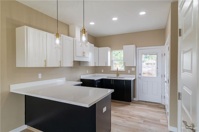 kitchen featuring white cabinets, sink, decorative light fixtures, light hardwood / wood-style floors, and kitchen peninsula