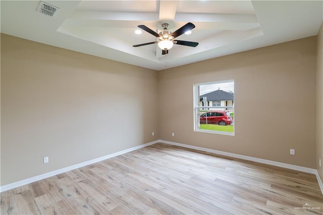 unfurnished room with ceiling fan, light hardwood / wood-style floors, and a tray ceiling