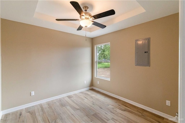 unfurnished room featuring light wood-type flooring, electric panel, a raised ceiling, and ceiling fan