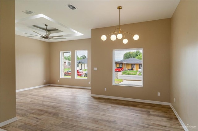 spare room with ceiling fan with notable chandelier, light hardwood / wood-style floors, and a tray ceiling